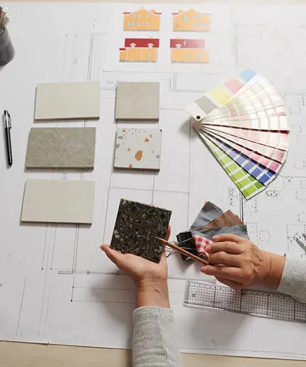 Technische Zeichnung einer Wohnung sowie verschiedene Farbmuster und Materialmuster liegen auf dem Tisch und werden verglichen.